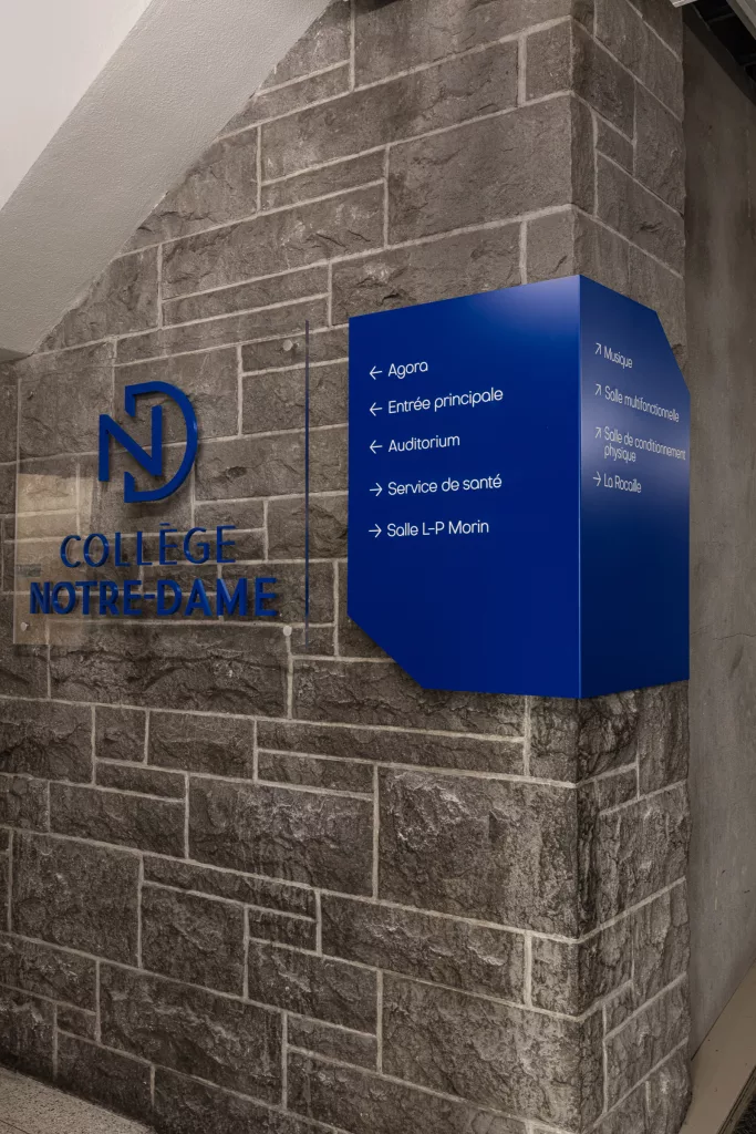 Détail de signalétique au Collège-Notre-Dame. On y voit le logo ainsi qu'un panneau de repérage en aluminium plié et vinyle.