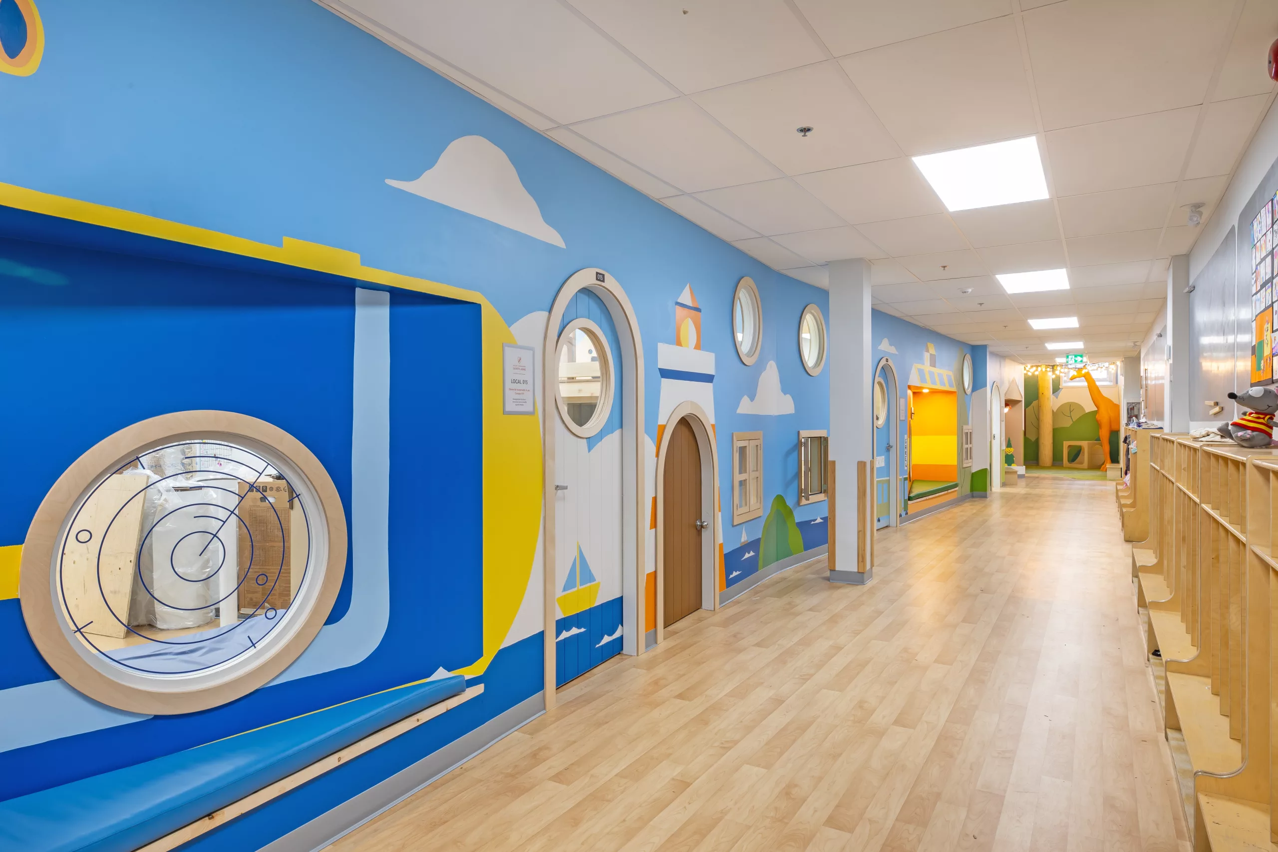 Vue générale du corridor au sous-sol du Collège Sainte-Anne Buissonnière. On y voit les portes de classes arrondies et la murale peinte à la main par Lucas Saenger.
