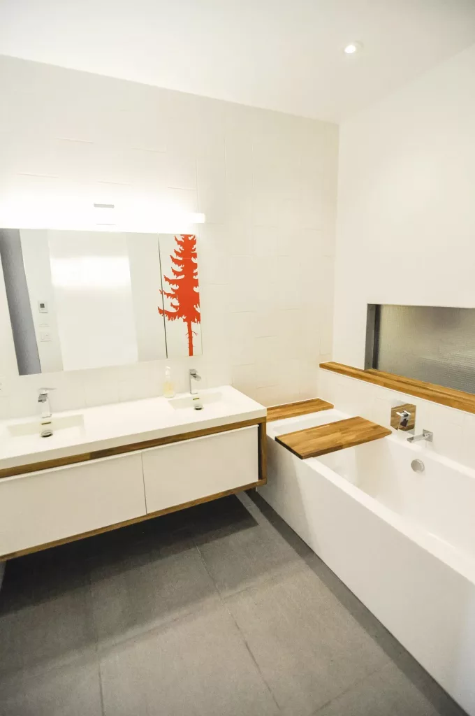 La salle de bain comprend majoritairement du blanc, mais est entrecoupée d'une couce de bois longitudinale.