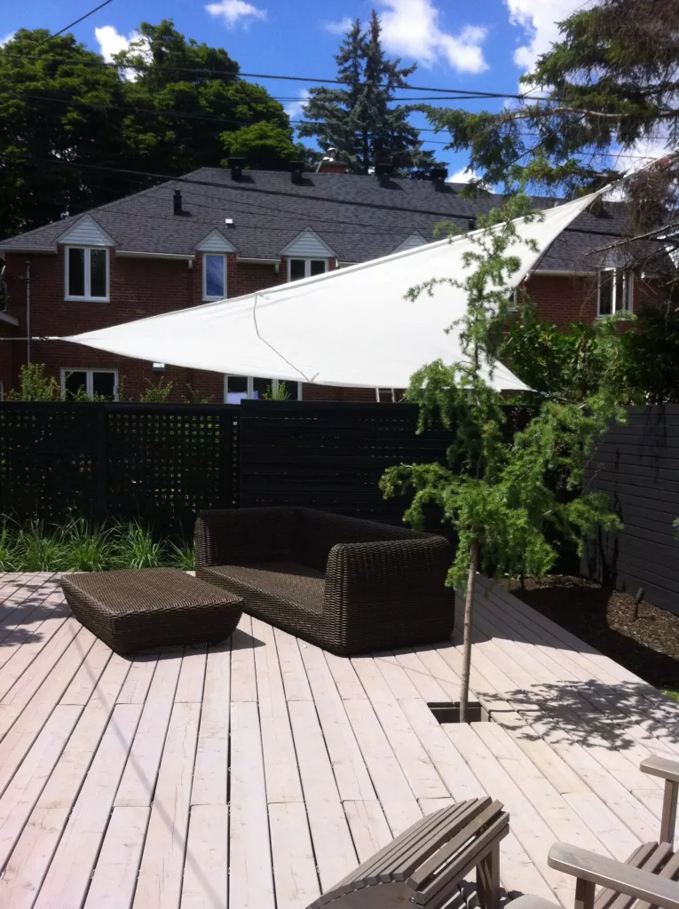 Vue de la partie arrière de la terrasse ou se trouve un mélèze ainsi qu'un sofa d'extérieur sous une voile d'ombrage.