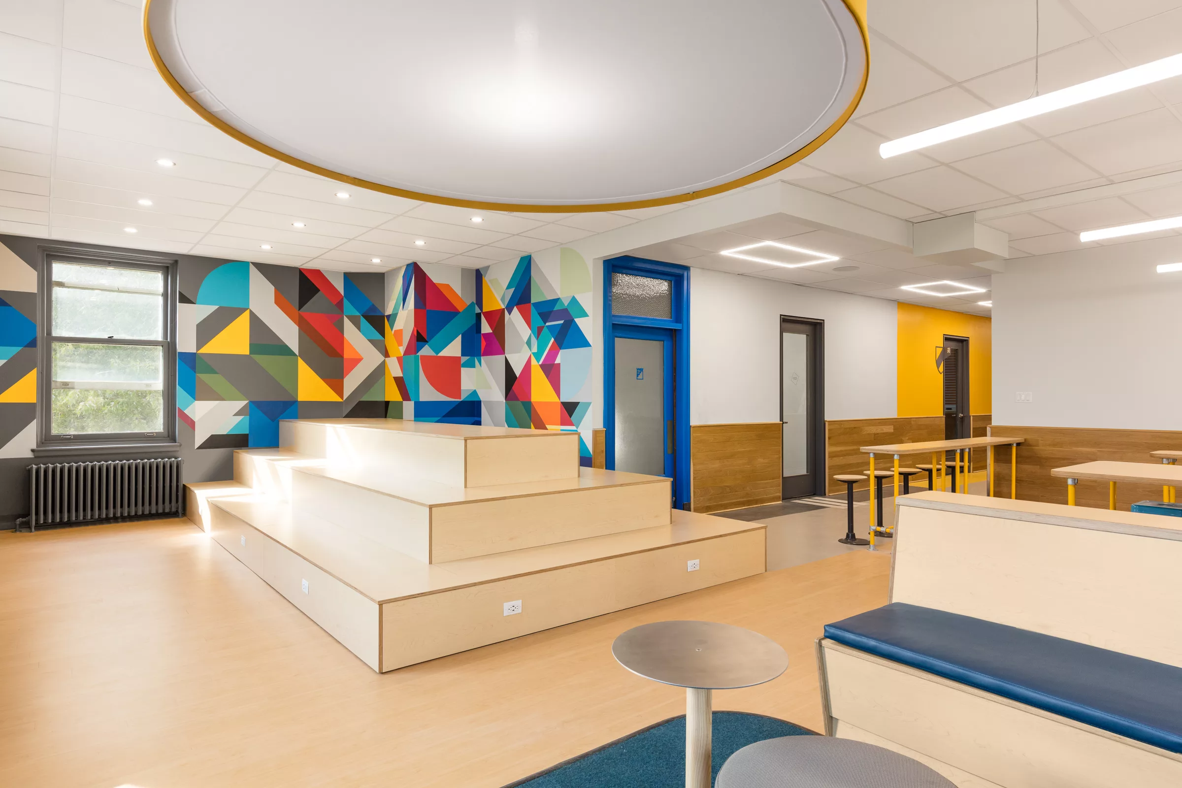 Une murale colorée dynamise les murs autour d'une estrade de bois clair dans l'espace commun du troisième étage du Collège Sainte-Anne.