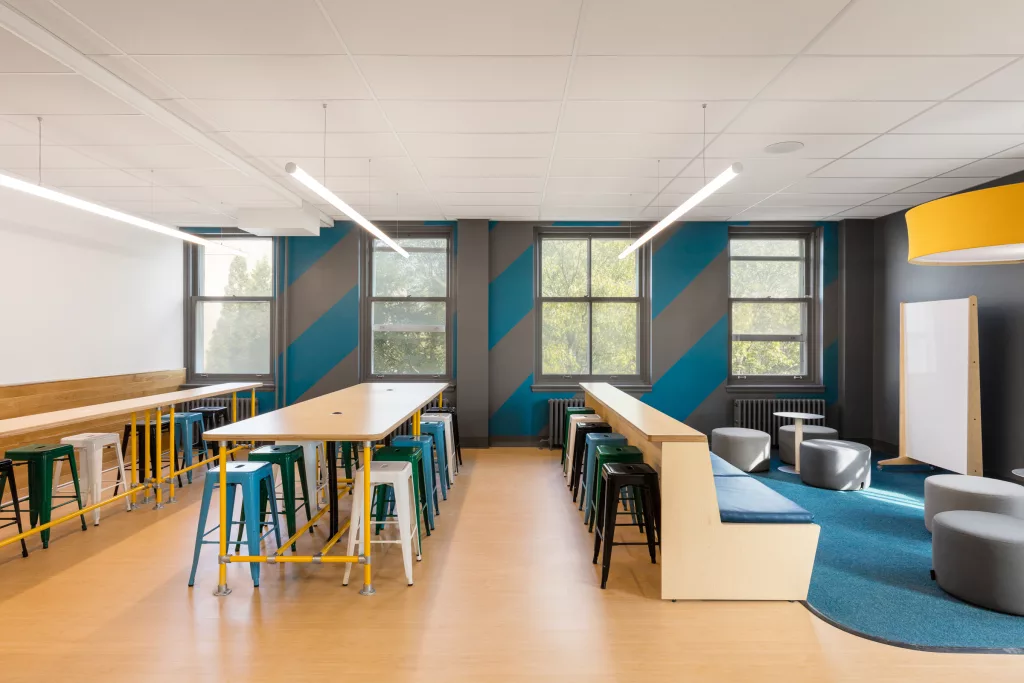 La salle commune du troisième étage du Collège Sainte-Anne est meublée de plusieurs comptoirs de travail en bois clair et de tabourets d'acier de couleurs différentes.