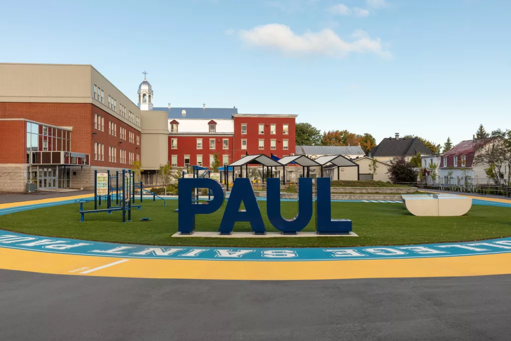 Le nom de Paul en lettres d'acier peint bleu sont disposé dans la partie active de l'espace gazonné de la cour extérieure du Collège Saint-Paul.