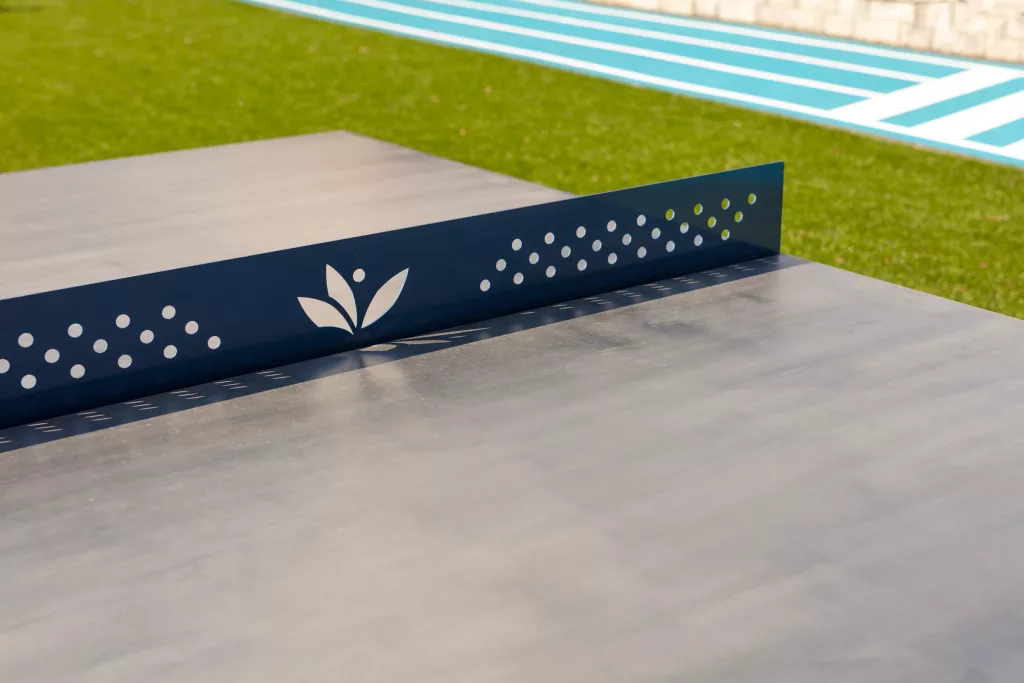 Un gros plan du filet en acier découpé d'une des table de ping-pong, ou le logo du Collège Saint-Paul est intégré au centre.