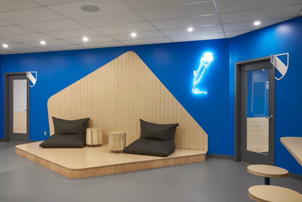 La scène de bois clair adjacente à des lattes de bois installées au mur contient deux fauteuils poires et des tables en forme de buches de bois sur roulettes.