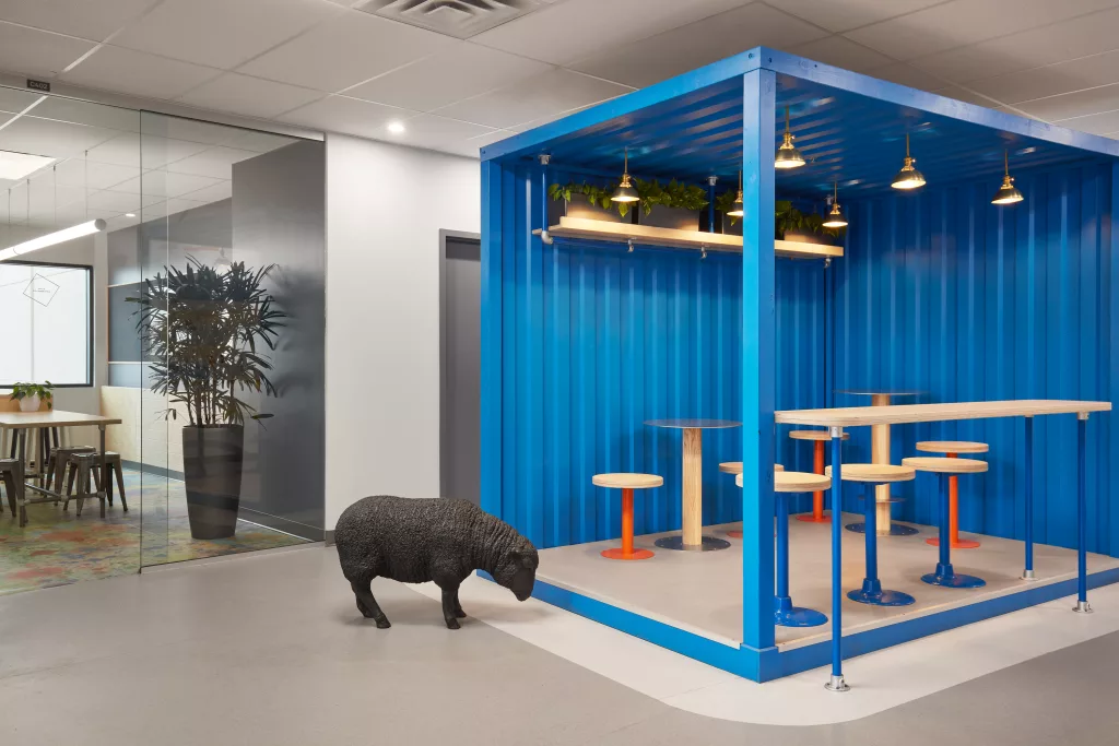 Une sculpture de fibre représentant un mouton se tient à côté d'un espace de travail mixte disposé dans une portion de conteneur bleu ouvert sur deux côtés.