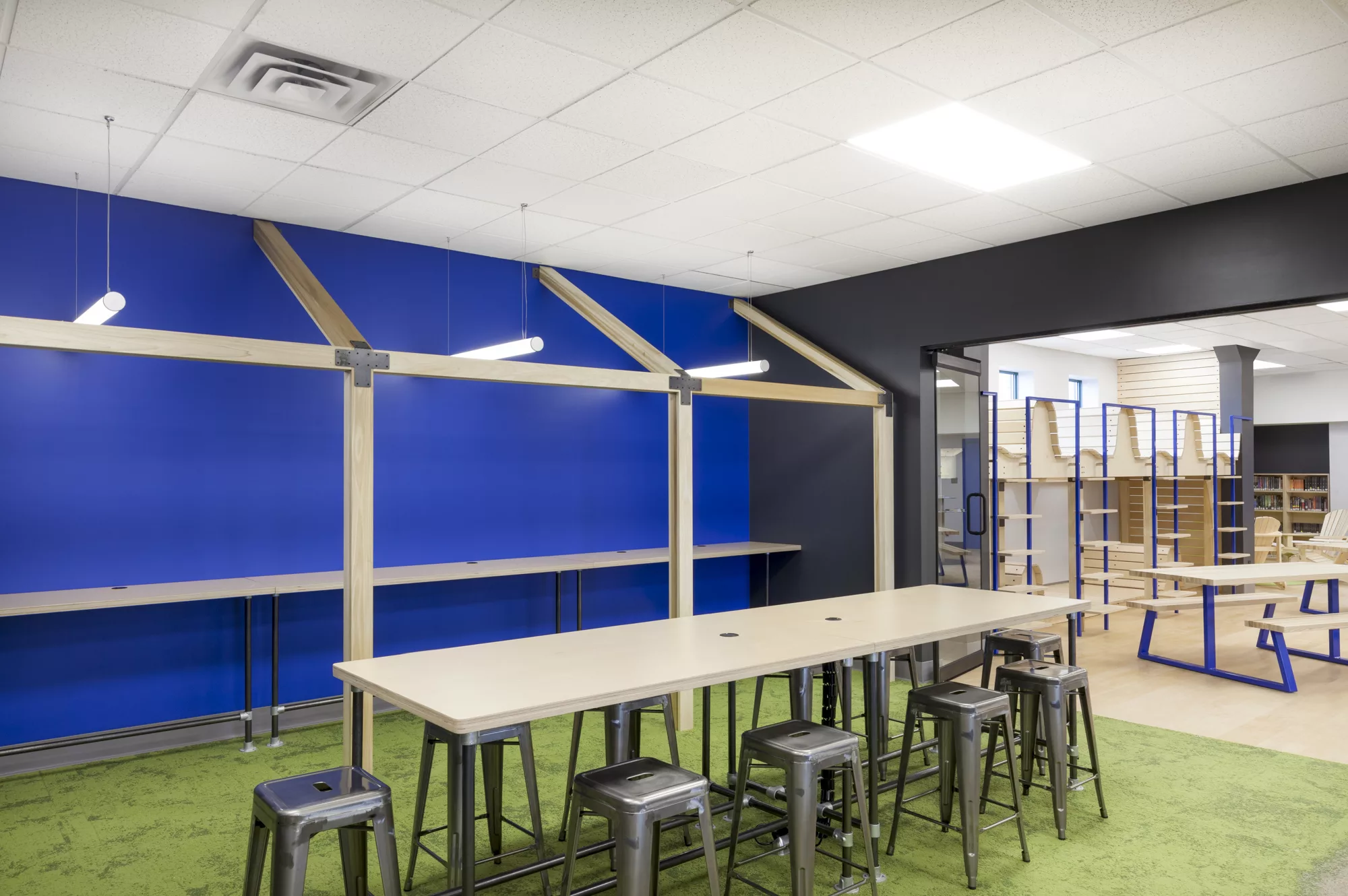 Vue d'une des salles de travail. Une grande table de travail centrale, ainsi qu'une structure en bois qui vient créer des bureaux hauts.