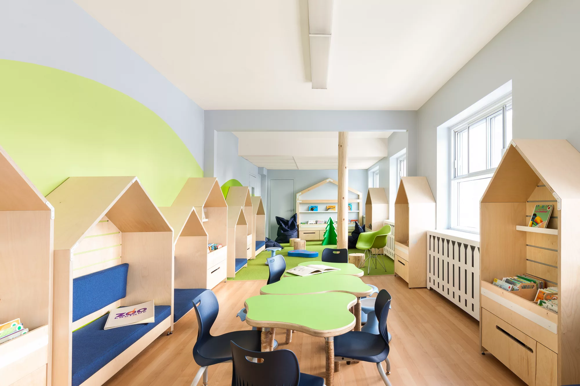 Vue générale de la bibliothèque du Collège Ville Marie à Montréal. Un aménagement lumineux avec des couleurs naturelles et du bois clair. De petites cabanes en bois servent d'étagères pour les livres et de banquettes.