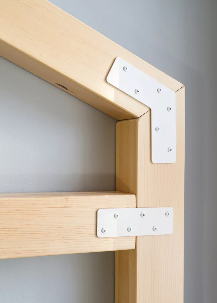Gros plan sur une partie du mobilier de la bibliothèque. On utilise des équerres métalliques pour assembler les morceaux de bois.