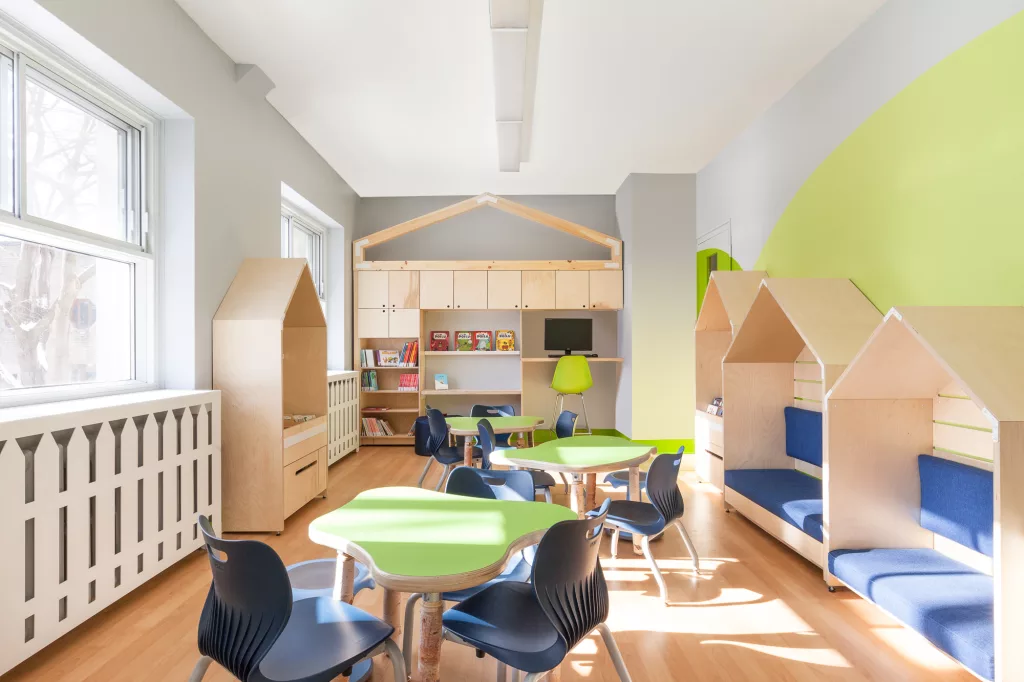 Vue générale de la bibliothèque du Collège Ville Marie à Montréal. Un aménagement lumineux avec des couleurs naturelles et du bois clair. De petites cabanes en bois servent d'étagères pour les livres et de banquettes. Des rayons de soleil amènent une lumière naturelle.