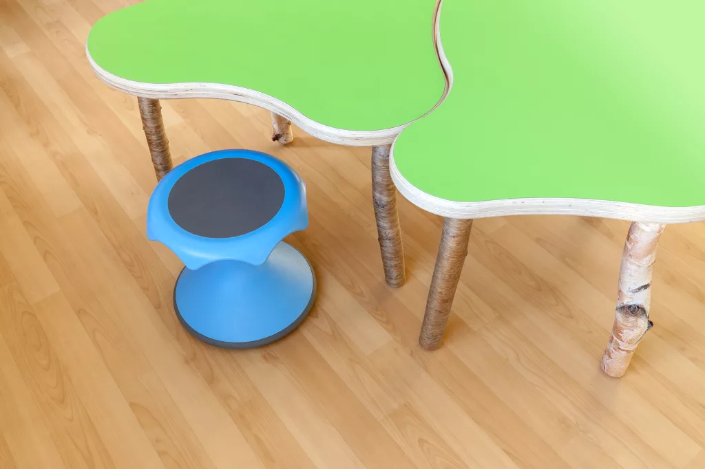 Vue rapprochée des tables de la bibliothèque. On y voit des tables avec des formes organiques vertes qui s'imbriquent, ainsi qu'un tabouret bleu.
