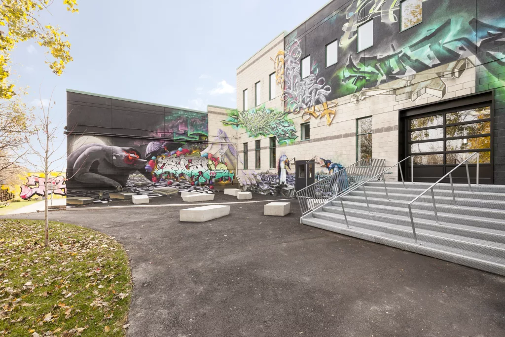 Des bancs de béton sont déposés devant des murs couverts de  graffitis d'artistes Montréalais et internationaux à gache de l'entrée des élèves du Collège Ville-Marie.