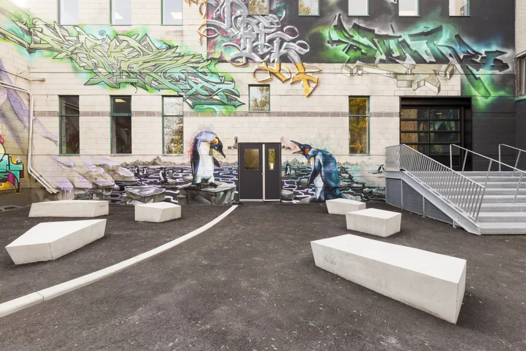 Des bancs de béton sont déposés sur l'ashpalte à gauce de l'entrée de la cour extérieur du Collège Ville-Marie.