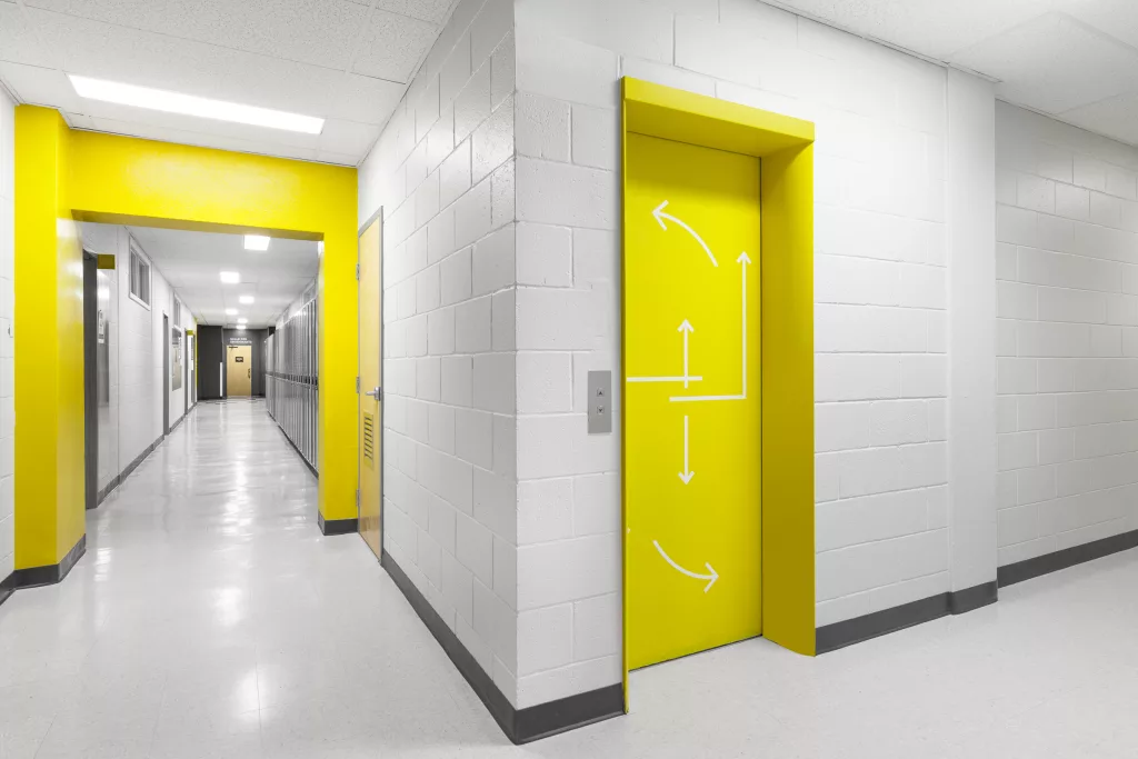 Vue d'un coin ou une arche et la porte d'ascenseur sont accentués de jaune.