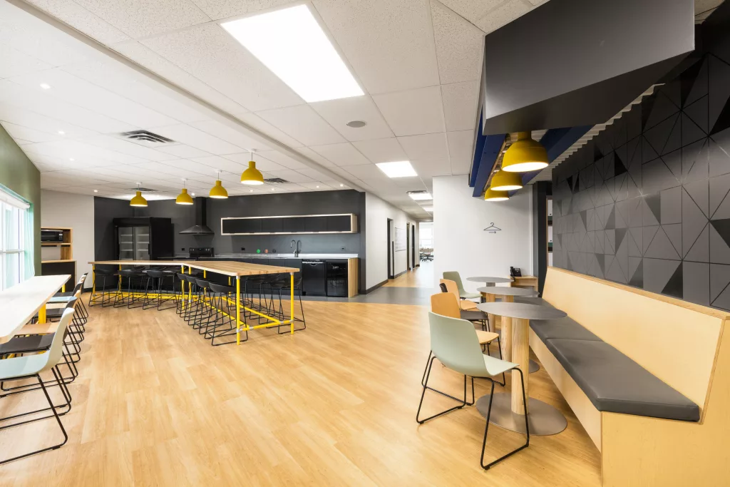 L'espace cuisine comprend des banquettes, du mobilier modulable, des électroménagers modernes et des lampes industrielles colorées suspendues.