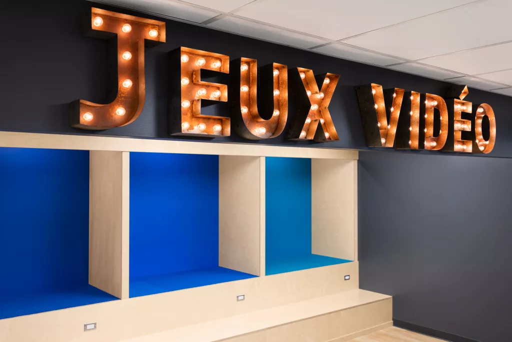 Le mur du haut des estrades comporte une enseigne en grosses lettres qui mentionnne ''Jeux Vidéos''.
