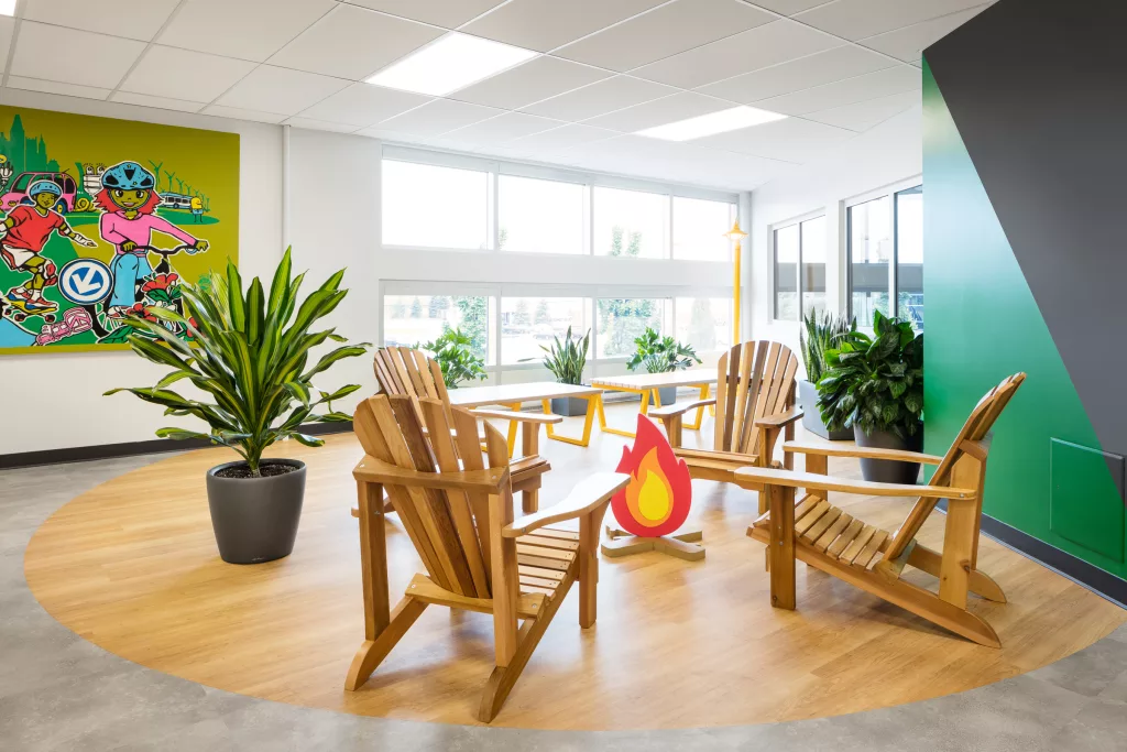 Un espace de lecture sur chaise adirondacks de bois dans la bibliothèque du Collège d'Anjou, comprenant un faux feu de camp fait de mousse et des plantes d'intérieur.