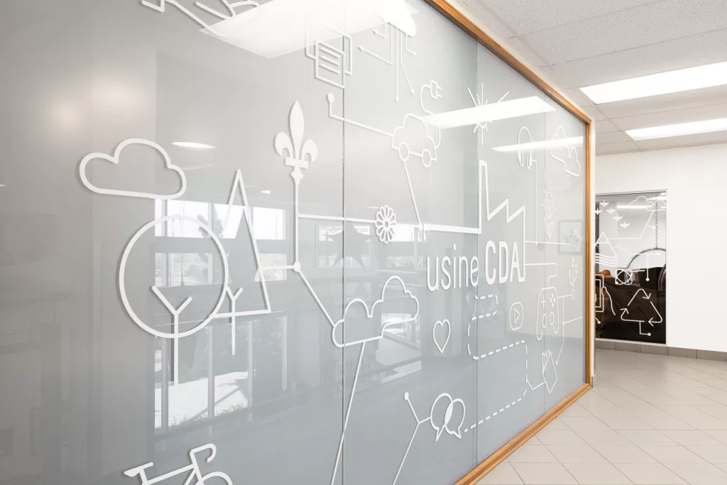 Un mur vitré est décoré d'une pièce graphique montrant les diverses fonctionnalités de la nouvelle bibliothèque du Collège d'Anjou, aussi appelé usine CDA.