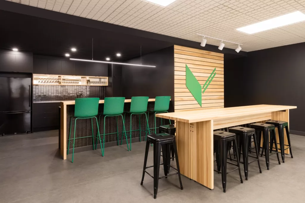 La salle multifonctionnelle Le Belvédère de l'Externat Sacré-Coeur comprend un comptoir de cuisine avec un lavabo, ainsi qu'un ilot de style comptoir en bois clair et une grande table dde bois.