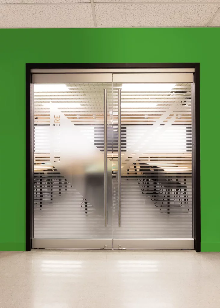Le portes vitrées de la salle multifonctionnelle Le Belvédère de l'Externat Sacré-Coeur comprennent le logo  glacé de l'établissement.