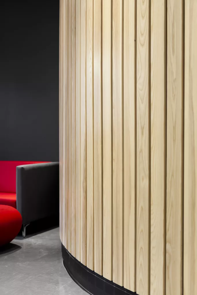 Des lattes de bois disposées verticalement sur un mur rond de l'aménagement créé par Taktik design.