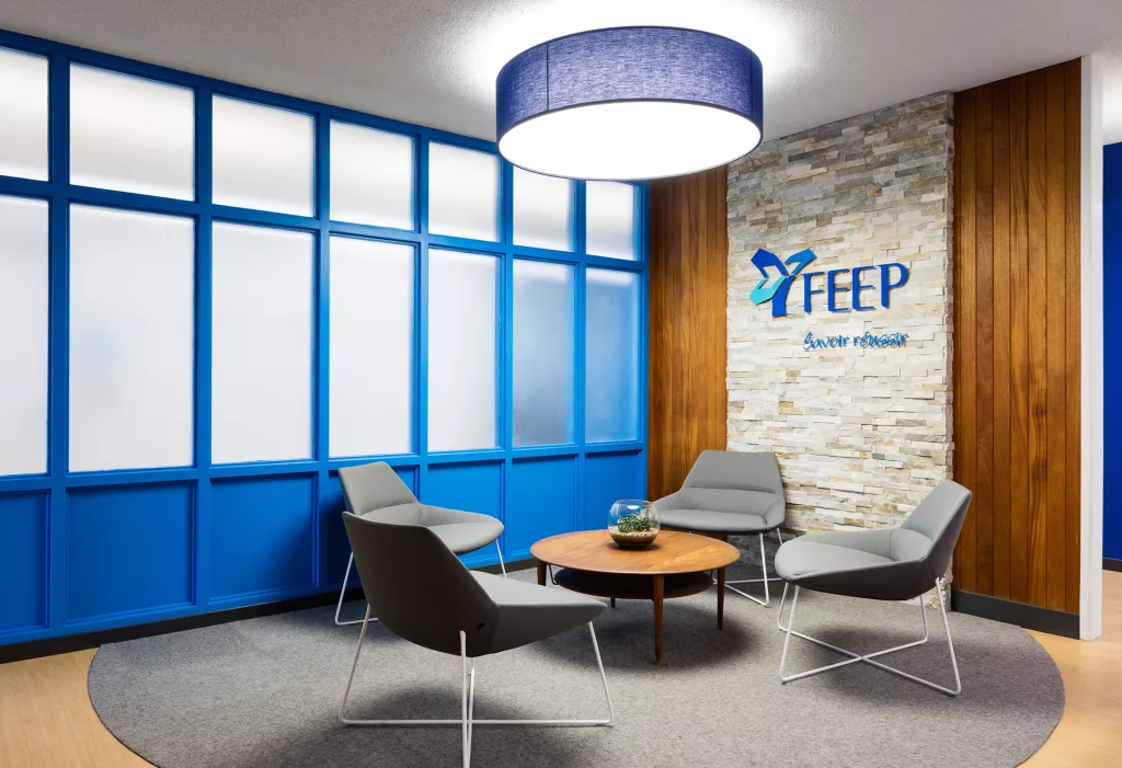 La salle d'attente de l'entré.e de l'édifice à bureaux de la FEEP à un mur vitré et un autre mur de merisier et de pierres, ou se retrouve le logo de l'institution.