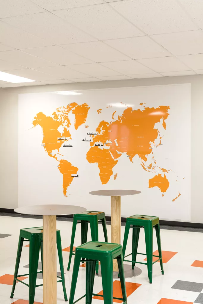 Des tables hautres de bois et de métal sont disposées devant une carte du monde aux couleurs de l'école Lucien-Guilbault.