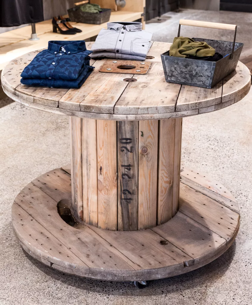 Une immense bobine de bois sur roulettes convertie en présentoir de vêtements dans la boutique l'Épingle à linge.
