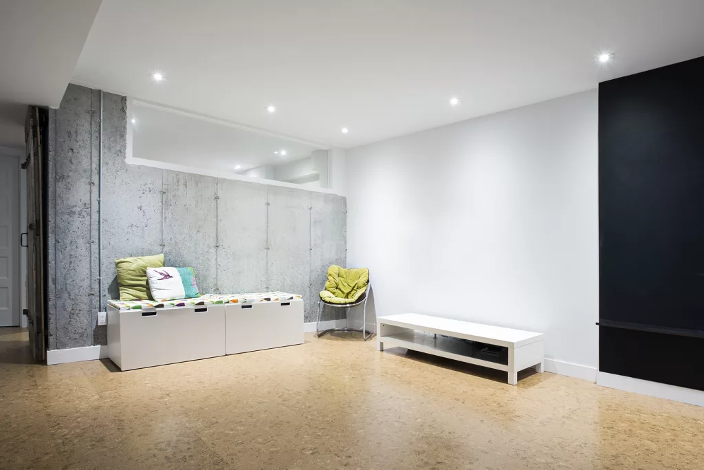 Le sous-sol de la résidence comprend un mur de béton ou s'insère une vitre dans le coin supérieur droit.