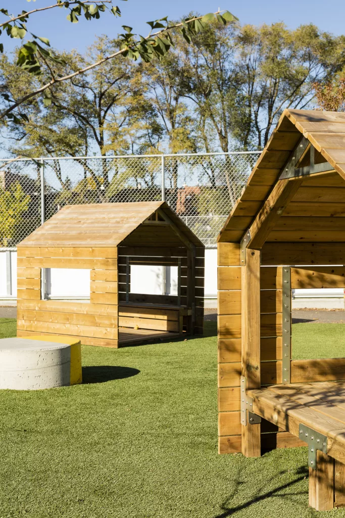 Quelques cabanes de bois posées sur un espace de gazon synthétique où les enfants peuvent jouer.