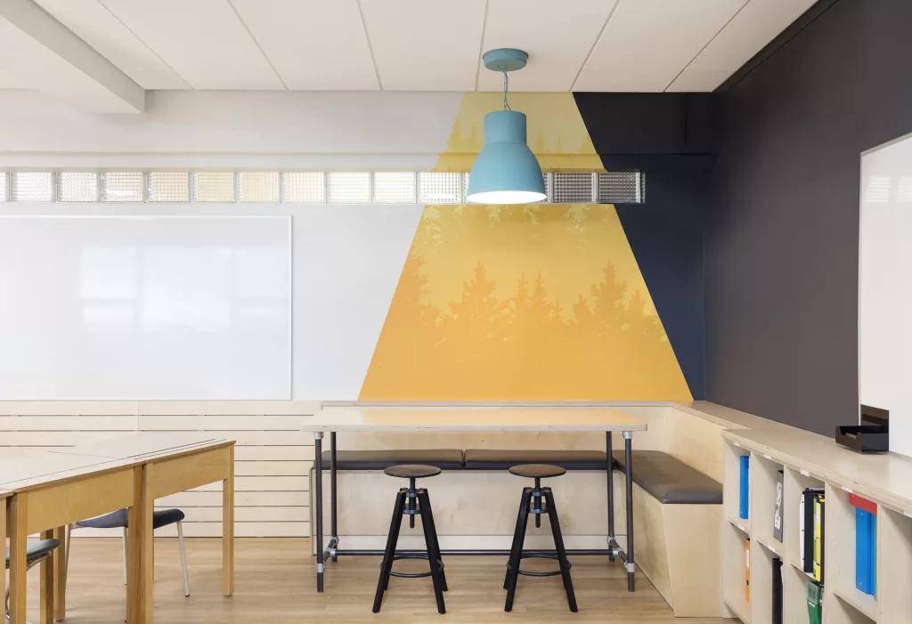 Un cpin de la classe aux murs colorés ou se trouve une banquette et des tabourets.