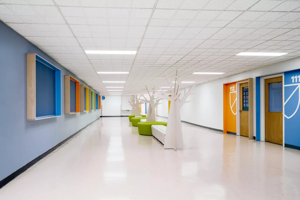 Un couloir de l'Académie Sainte-Anne comprenant des bancs colorés et des cadres destinés aux différents élèves.