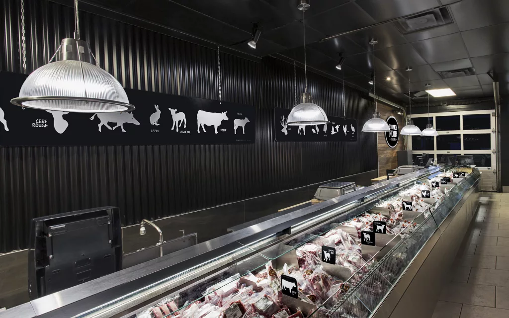 Le comptoir réfrigéré de la boucherie Le Prince Noir est éclairée de lampes suspendues afin de donner un éclat incomparable aux coupes de viandes.
