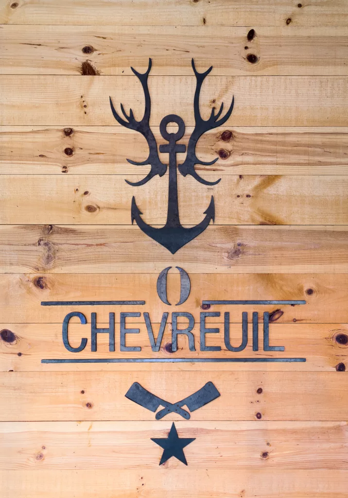 Une murale de pièces d'acier sur un mur de bois clair représentant une armoirie du restaurant O'Chevreuil.