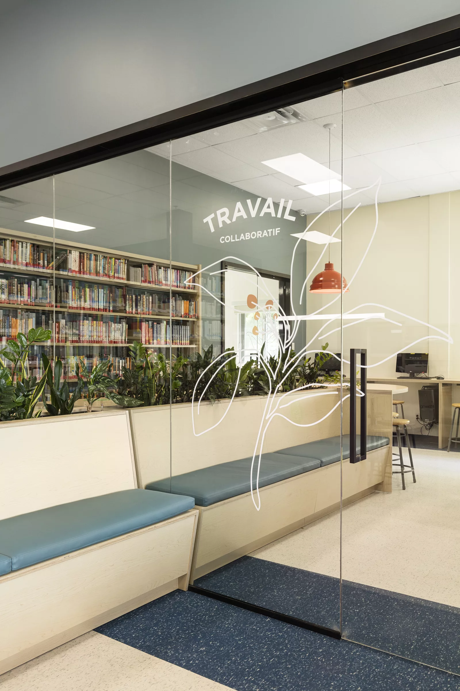 Une vue de la bibliothèque du Collège Saint-Hilaire, vers la salle de travail vitrée. On ny voit une intervention en vinyle sur la vitre.
