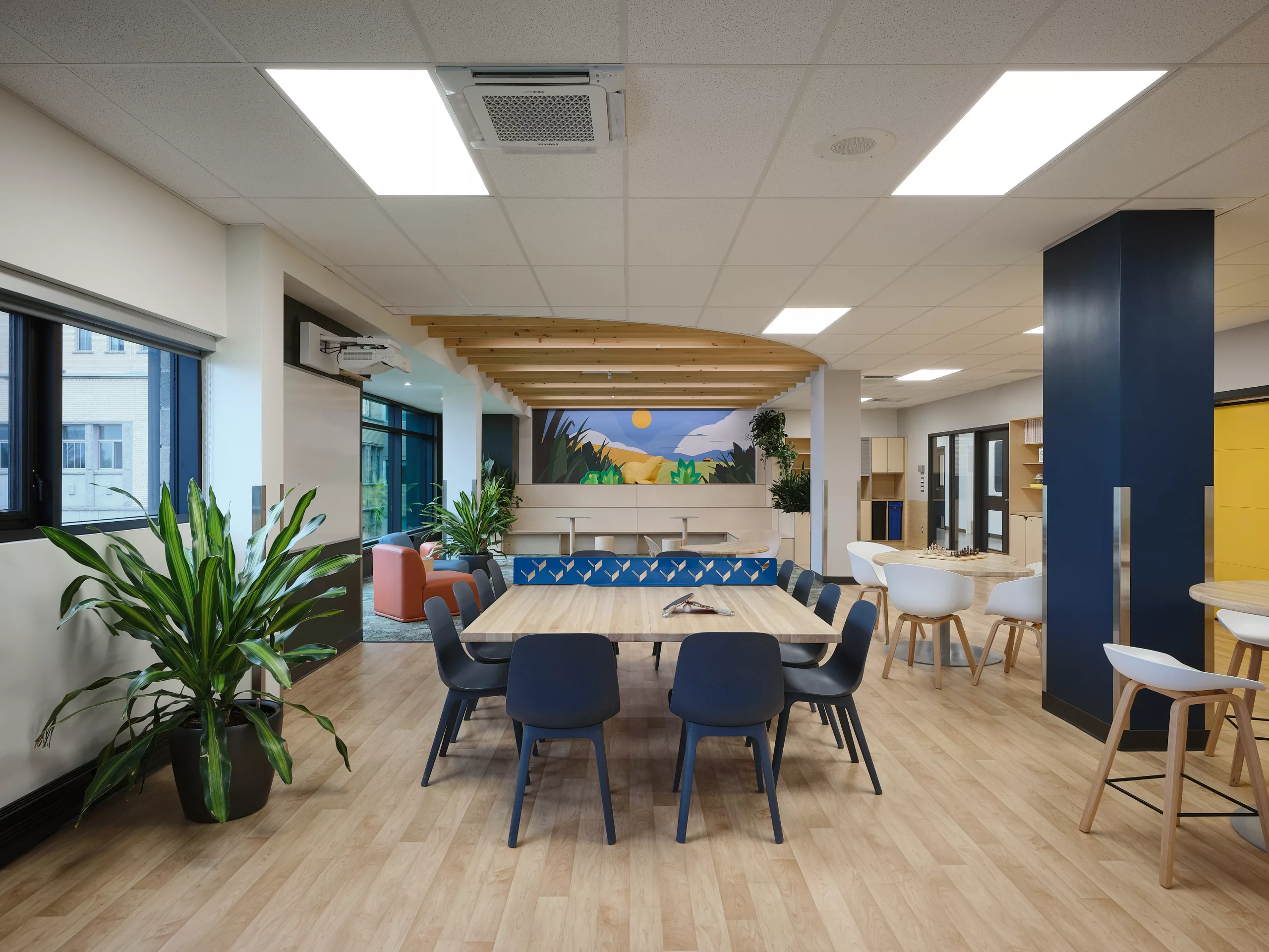 Vue de la salle commune du pavillon sportif de l'Externat Sacré-Coeur. On y voir les différents espaces de travail ainsi qu'une estrade décorée d'une murale.