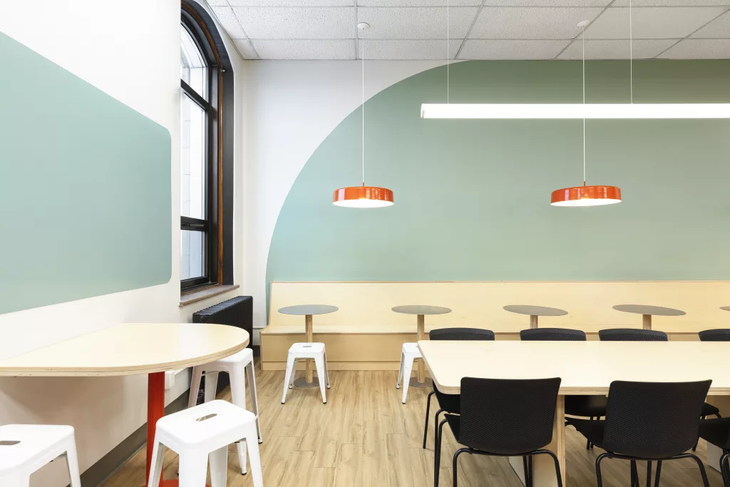 Des murs peints de formes de couleurs géantes, des lampes suspendues oranges, une banquette de bois, des tables rondes font partie du design des classes flexibles du Pensionnat du Saint-Nom-de-Marie.